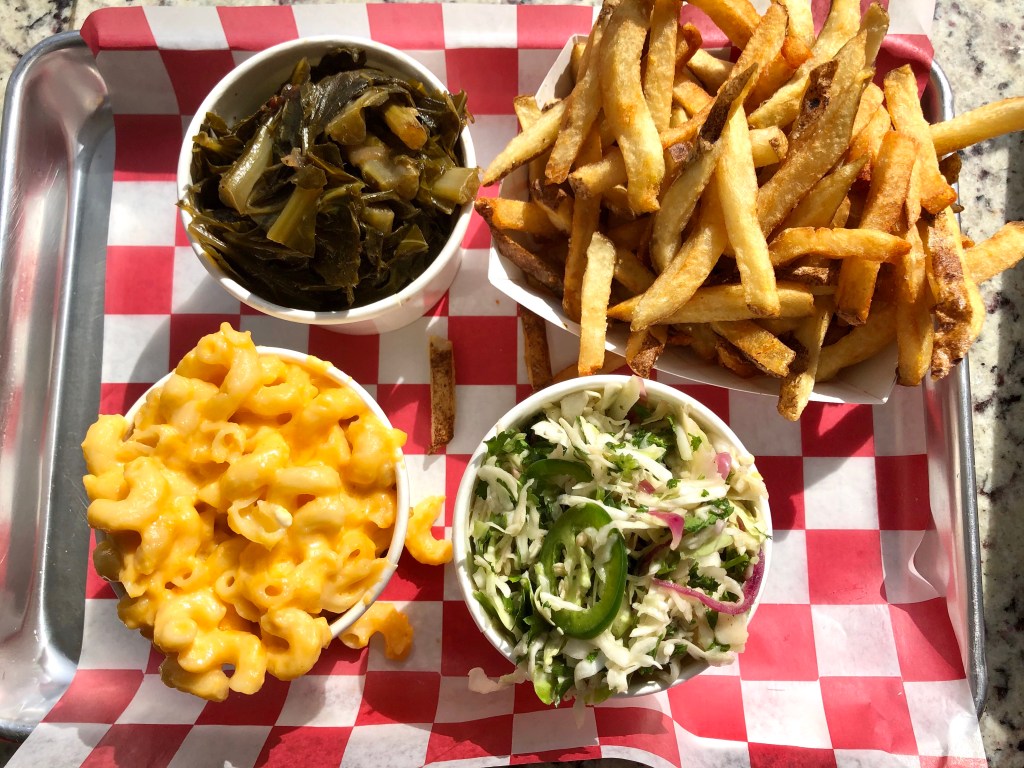 Roaming Rooster’s sides: collard greens, fries, macaroni and cheese, and coleslaw. Roaming Rooster is a restaurant with multiple locations in the Washington, D.C. Metropolitan Area.