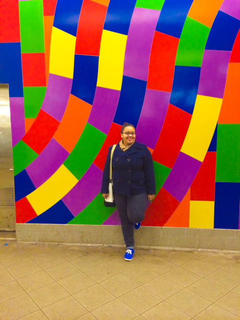 A woman standing in front of a subway mural.