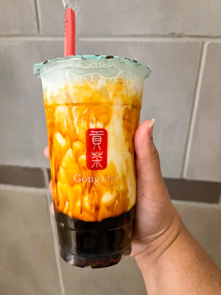 A hand holding a drink called Dirty Brown Sugar Latte with boba pearls at the bottom. This drink is from Gong cha, a bubble tea shop in the D.C. Metro Area.