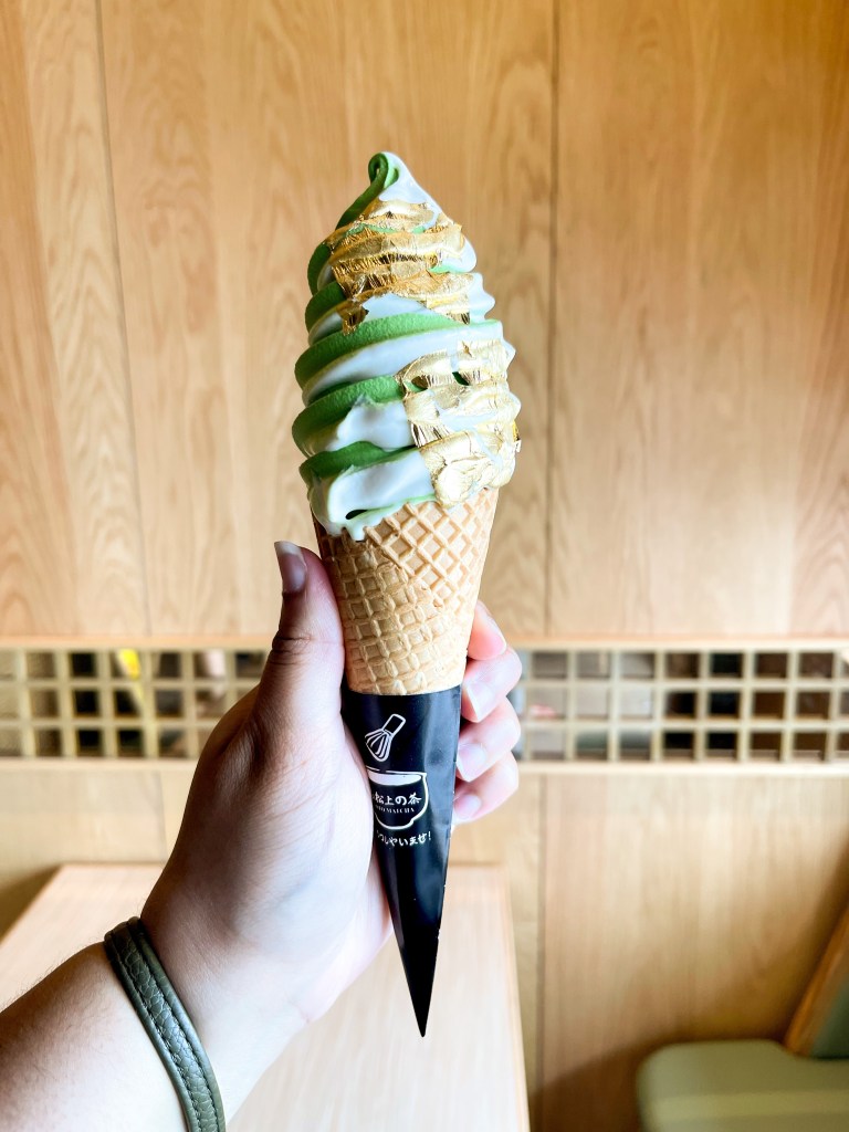 A hand holding an ice cream cone that has swirled ice cream. The flavors are matcha and milk. This photo was taken inside of Kyoto Matcha, a dessert shop in Ellicott City.