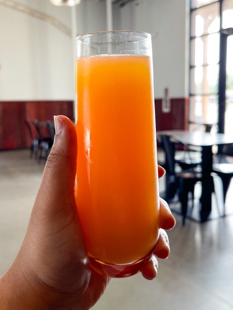 A hand holding a watermelon mimosa from the Hall CP, a restaurant located in College Park, Maryland