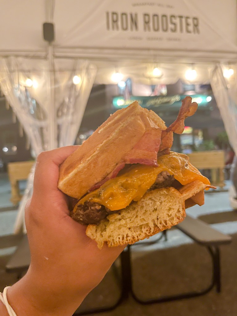 A hand holding a burger called a "waffle burger" at Iron Rooster, a restaurant with locations in Maryland.
