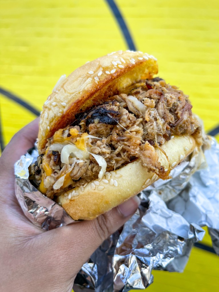 A hand holding a sandwich called "Big Cheese" from a restaurant called Federalist Pig. They have locations in Washington, D.C. and a food truck in Hyattsville, Maryland.