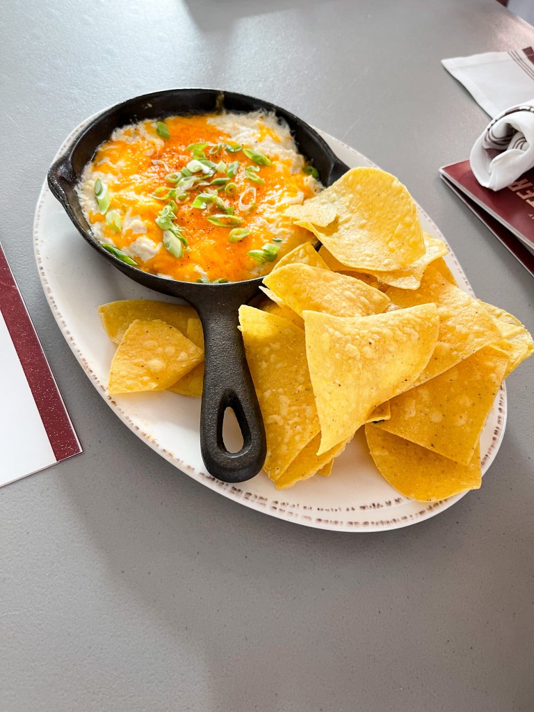 Maryland Crab Dip in a small cast iron skillet with tortilla chips on a plate. This appetizer is from Iron Rooster, a restaurant with locations in Maryland.
