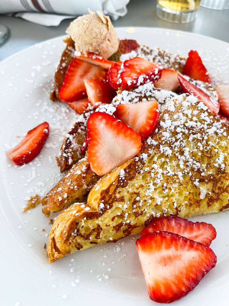 Brioche French Toast topped with strawberries, powdered sugar, and maple bourbon butter. This dish is from Iron Rooster, a restaurant with locations in Maryland.