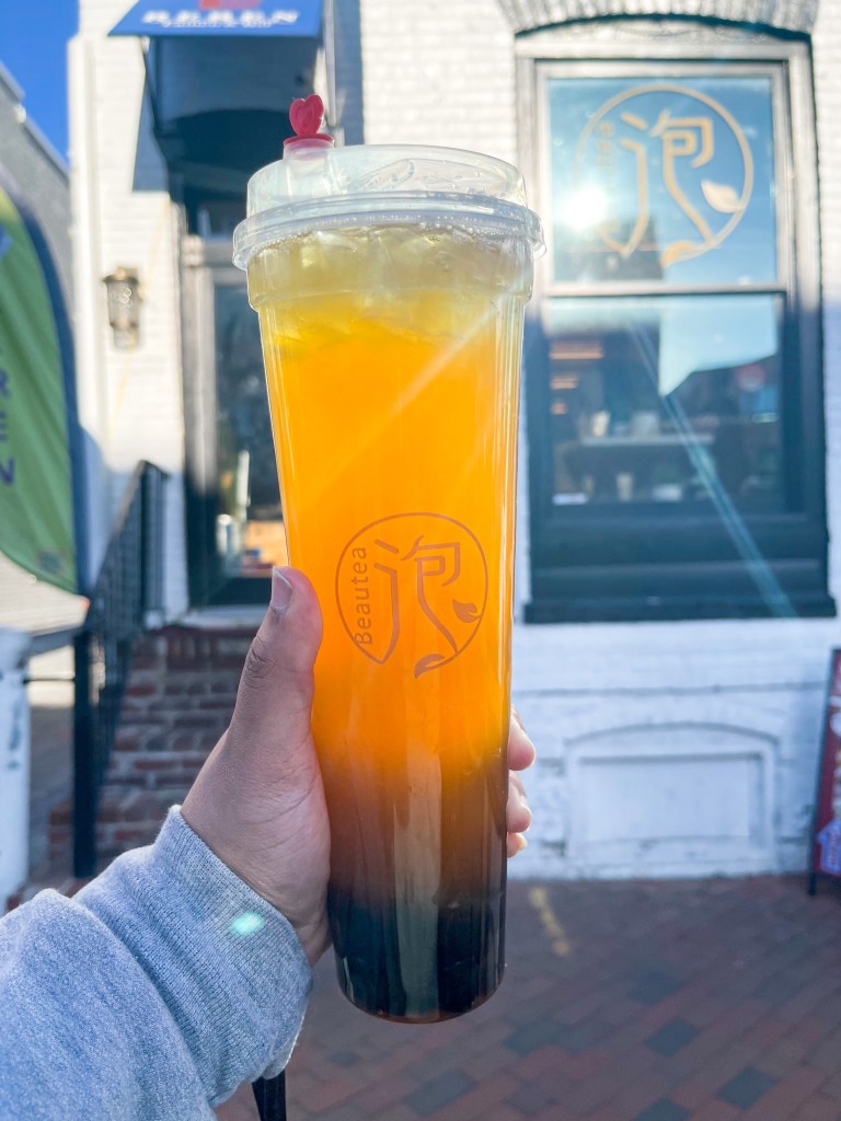 A hand holding a cup of iced passion fruit green tea from BeauTea, a bubble tea shop in Georgetown, Washington, D.C.