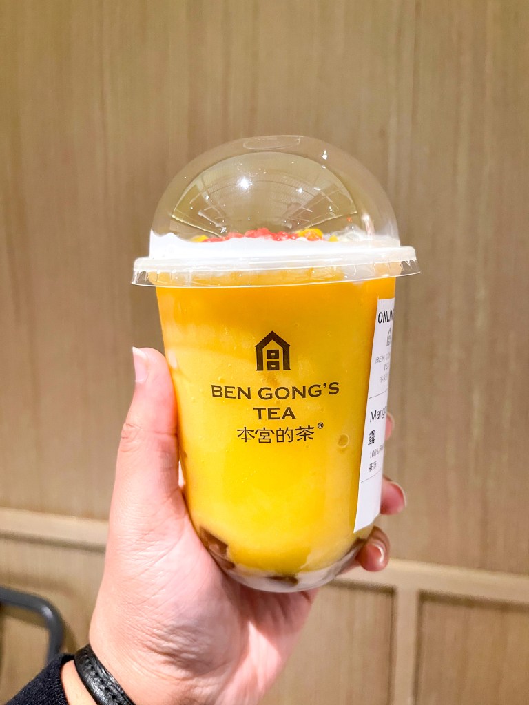 A hand holding a drink from Ben Gong's Tea, which is a bubble tea shop with locations in Maryland and Virginia. This drink is called "Mango Pomelo Sago."
