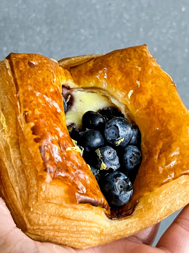 A hand holding a blueberry croissant tart from Sunday Morning Bakehouse