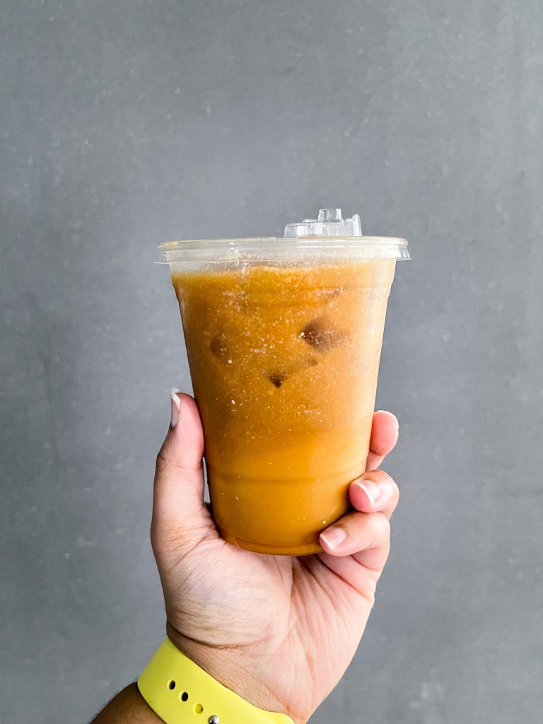 A hand holding a Caramel Cold Brew coffee from Sunday Morning Bakehouse, a cafe located in North Bethesda, Maryland