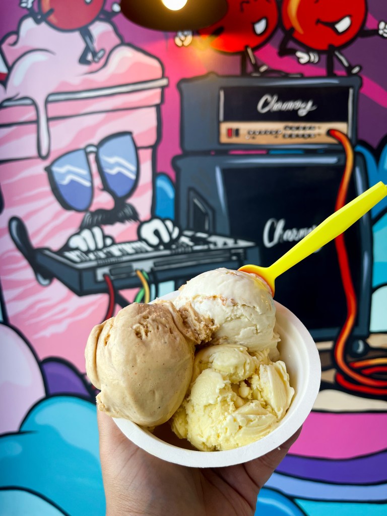 A hand holding a three-scoop bowl of ice cream from The Charmery in Columbia, Maryland. The flavors: Old Bay Caramel, Golden, Green Apple Curry