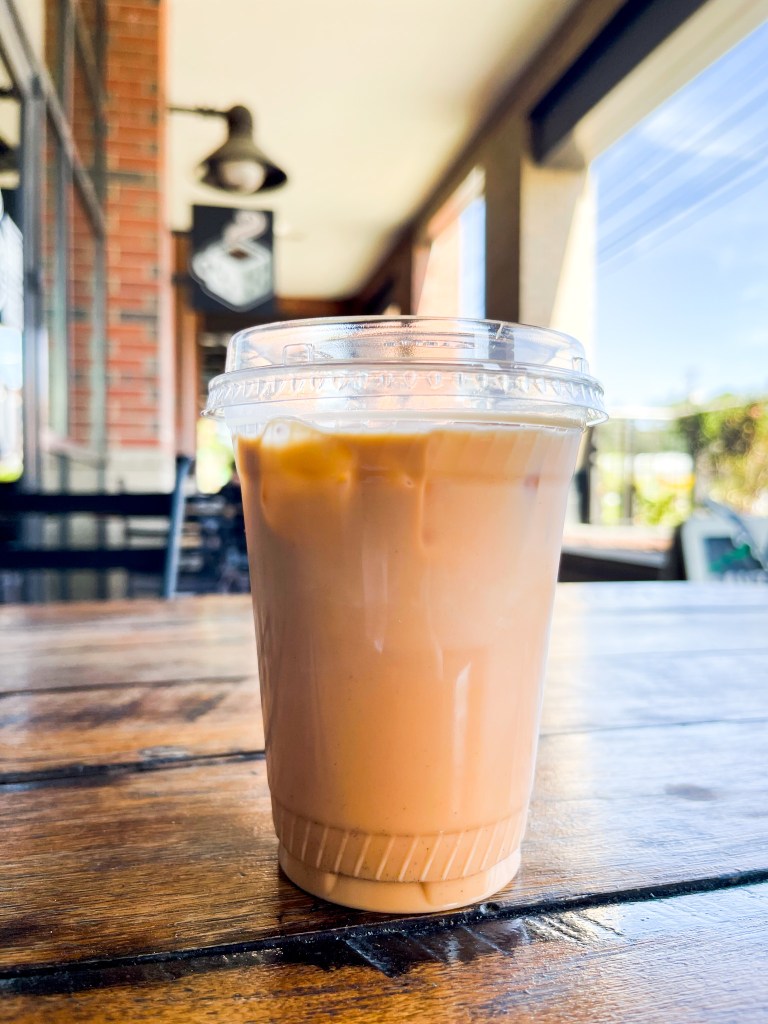 An iced latte sitting on a table. The latte is from the Board and Brew, which is a coffee shop in Maryland. The drink is called Black Thai.