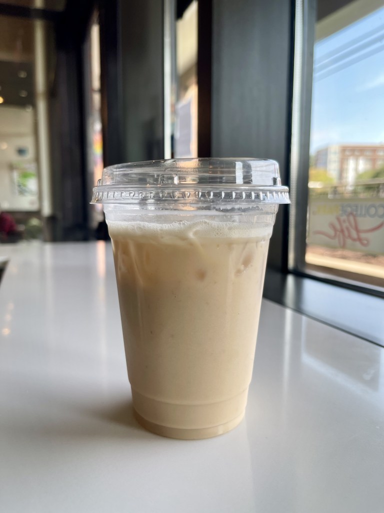 A drink in a plastic cup sitting on a countertop inside of a cafe