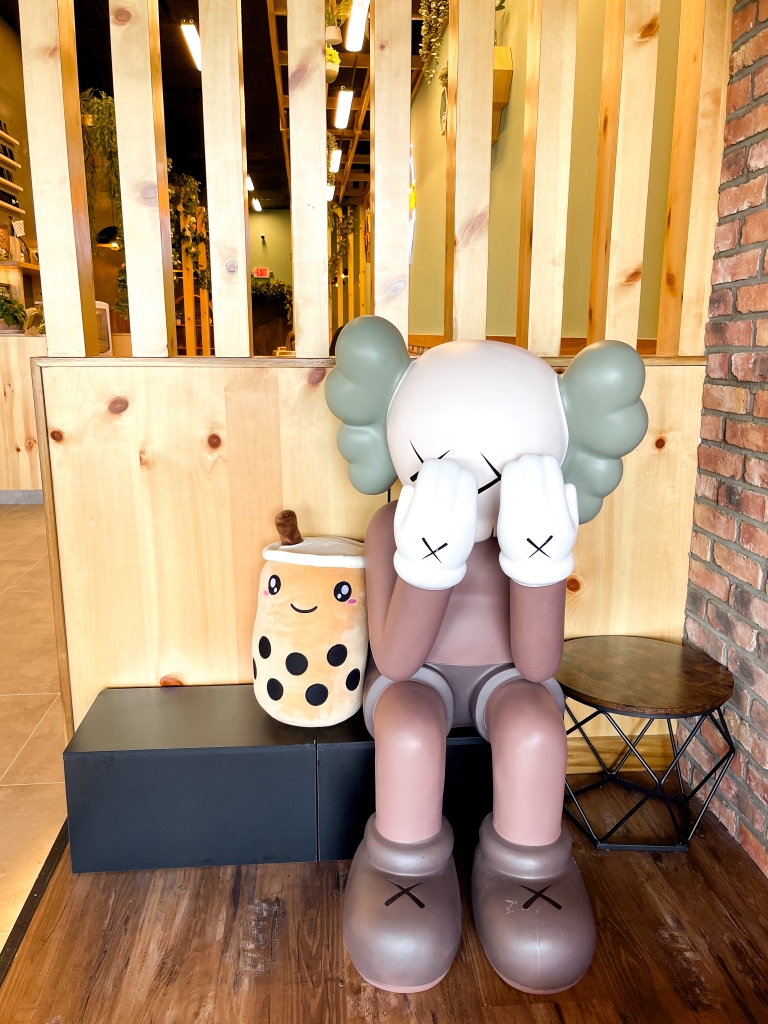 A stuffed animal and a sculpture sitting on a bench inside of a bubble tea shop
