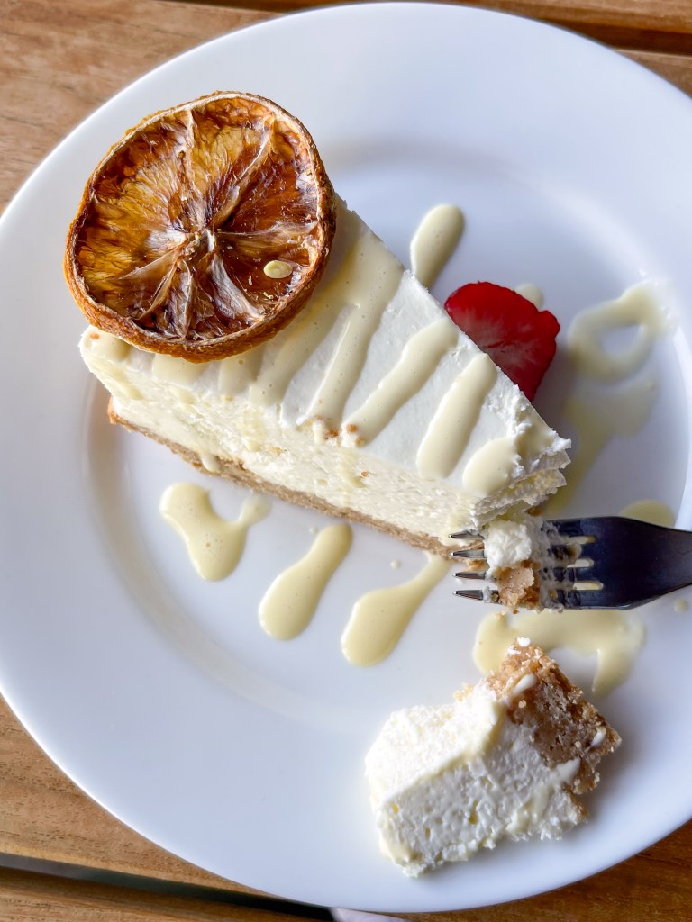 A slice of Limoncello Cheesecake with a dehydrated orange slice and lemon drizzle on top. This cheesecake is from Branch & Bird, a restaurant in Fort Worth, Texas