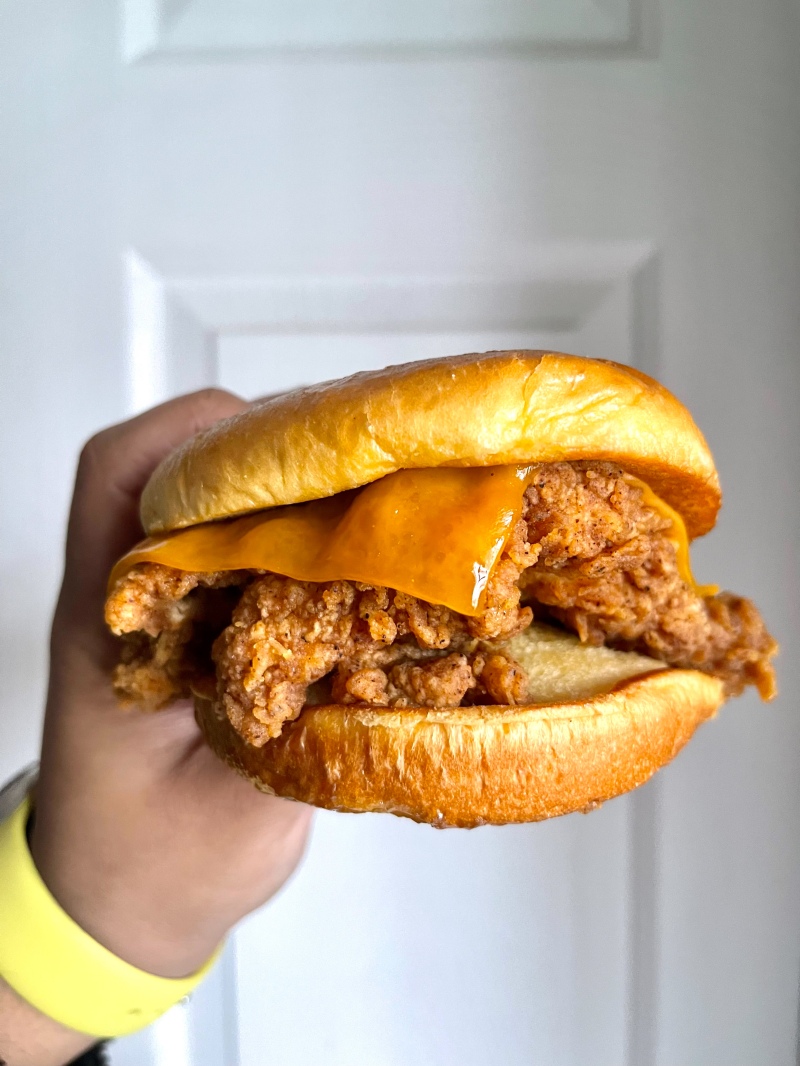 A hand holding a fried chicken sandwich that has cheese on top