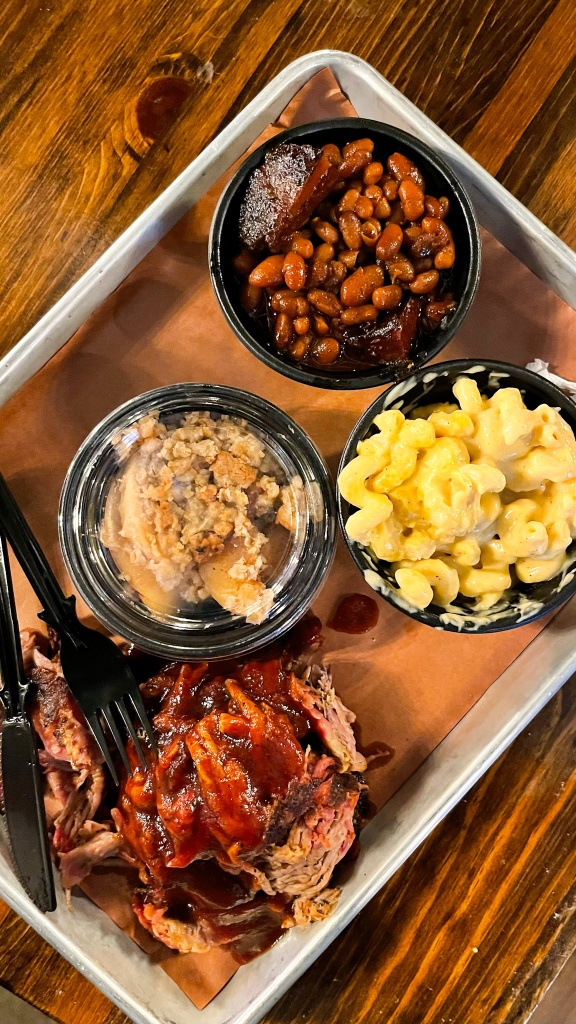 A tray with cups of baked beans, macaroni and cheese, apple crisp, and BBQ pulled pork