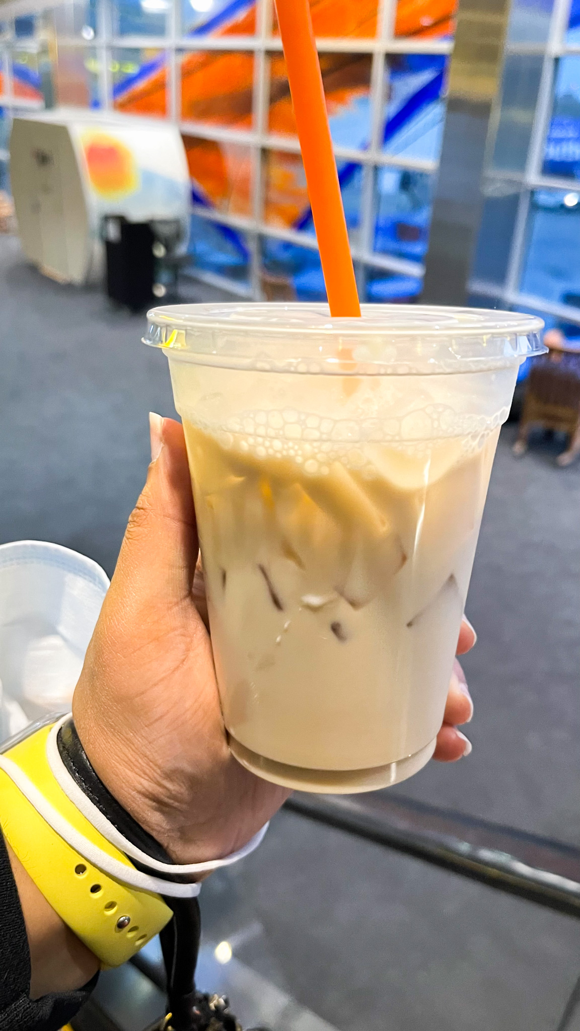 A hand holding an iced chai latte at the airport