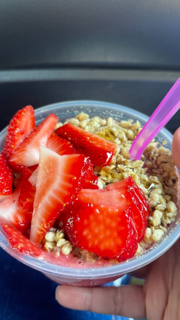 A hand holding a smoothie bowl topped with strawberries and granola