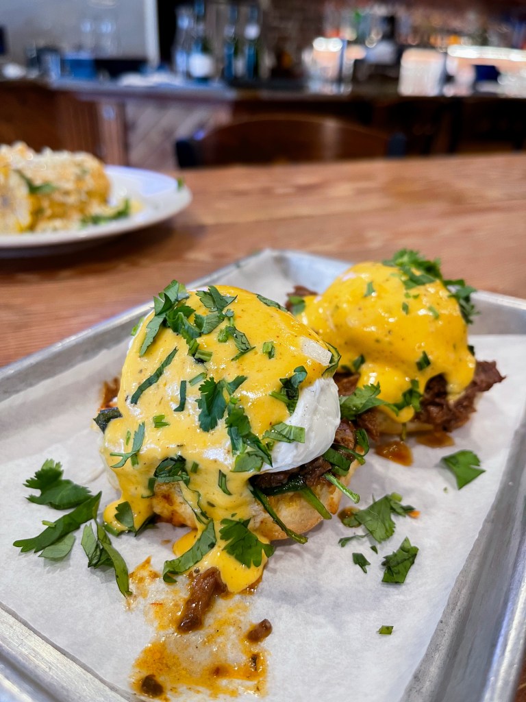 Two eggs Benedict sliders topped with barbacoa and poached eggs on a tray