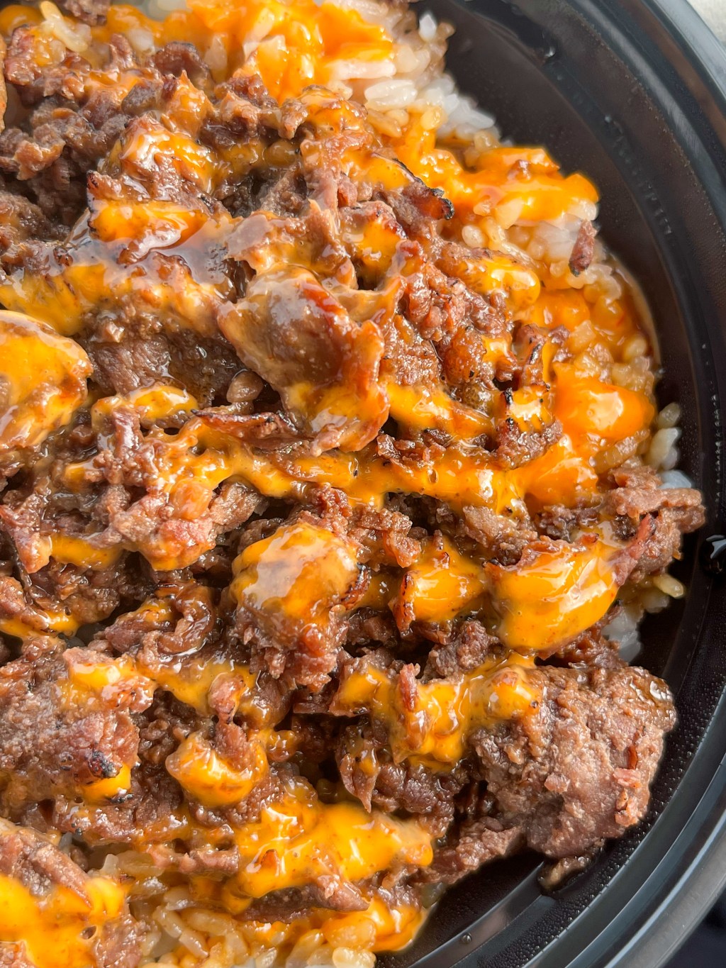 A bowl of beef and rice drizzled with sauce
