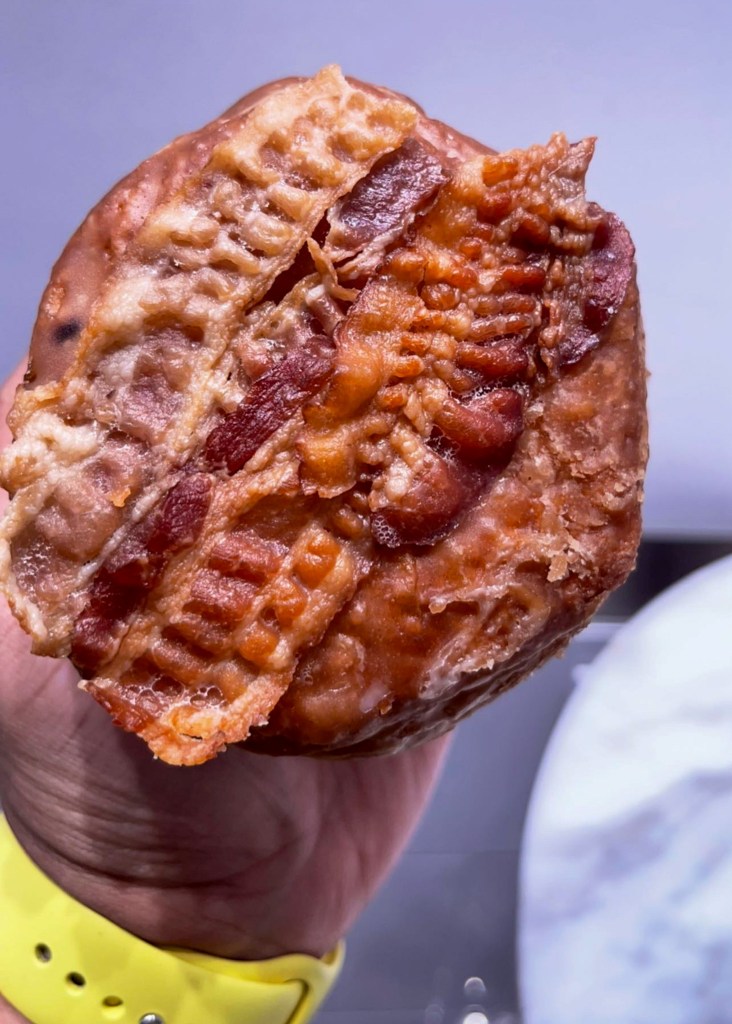 A hand holding a donut with strips of bacon on top