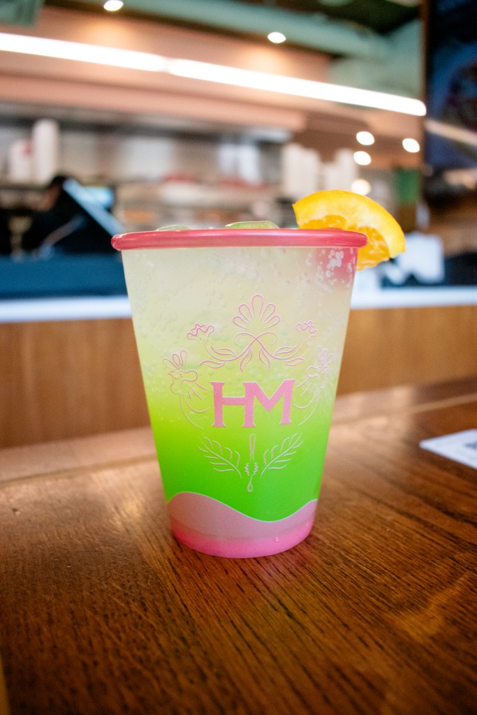 A green colored drink garnished with an orange slice sitting on a table