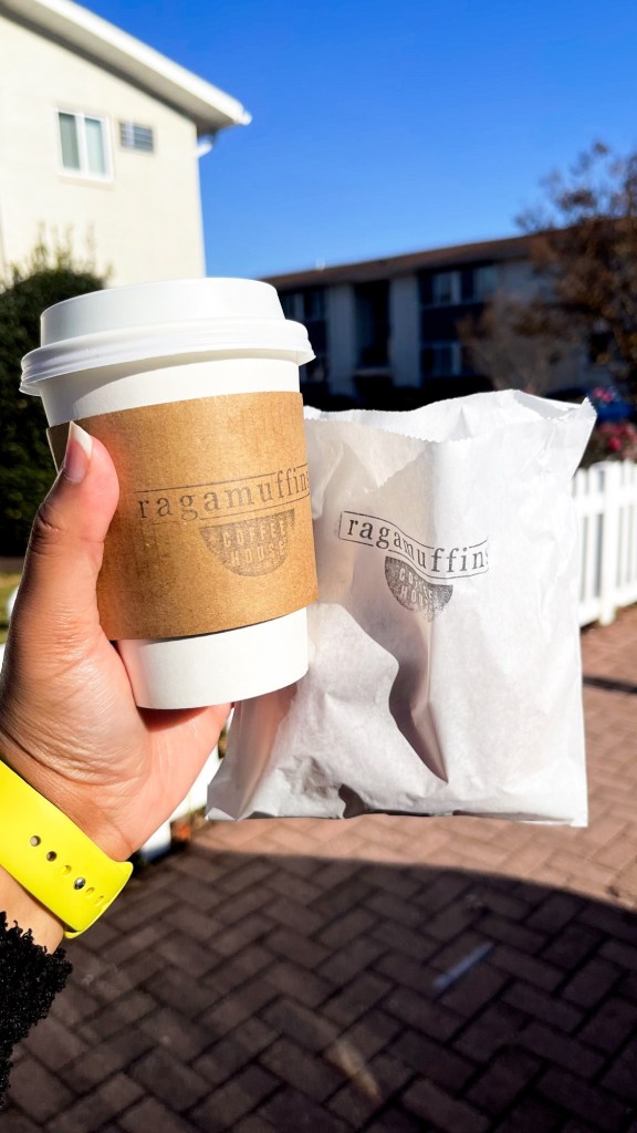 A hand holding a drink and a bag with a pastry in it