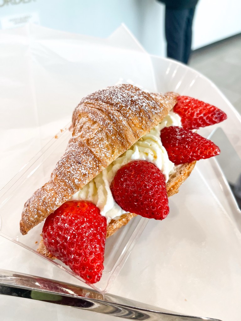 A croissant with cream and strawberries that is topped with powdered sugar
