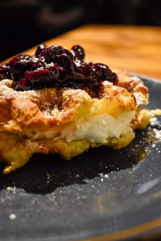 a crispy waffle dessert filled with lemon ricotta and topped with blueberries sitting on a plate